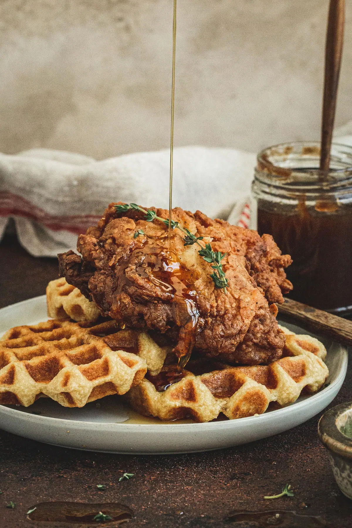 Syrup drizzling on fried chicken and waffles on a white plate.