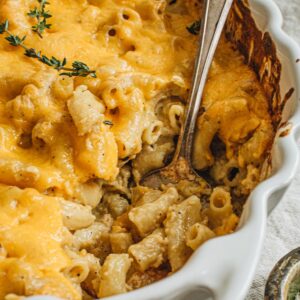 Baked mac and cheese in a white casserole dish with a silver serving spoon.