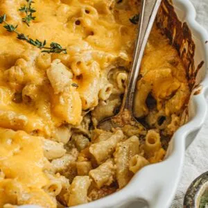 Baked mac and cheese in a white casserole dish with a silver serving spoon.