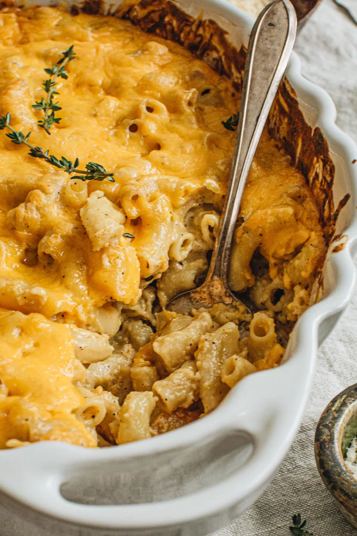 Baked mac and cheese in a white casserole dish with a silver serving spoon.