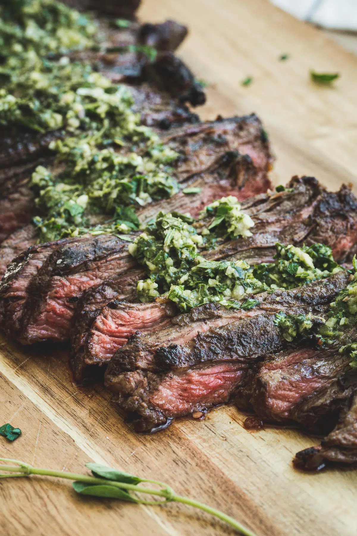 Churrasco on a wooden board topped with fresh chimichurri sauce.