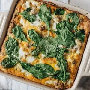 Egg breakfast casserole topped with spinach in a square baking dish.