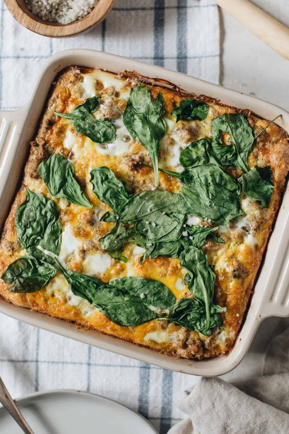 Egg breakfast casserole topped with spinach in a square baking dish.