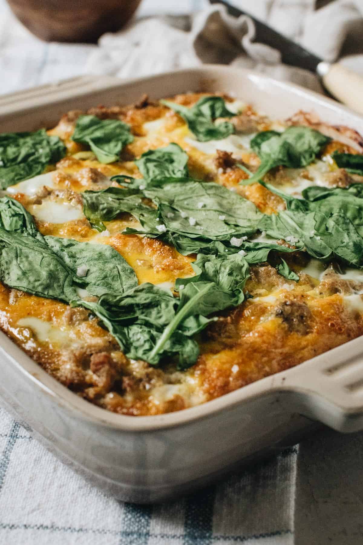 Turkey and egg breakfast casserole topped with spinach and coarse salt in a square baking dish.