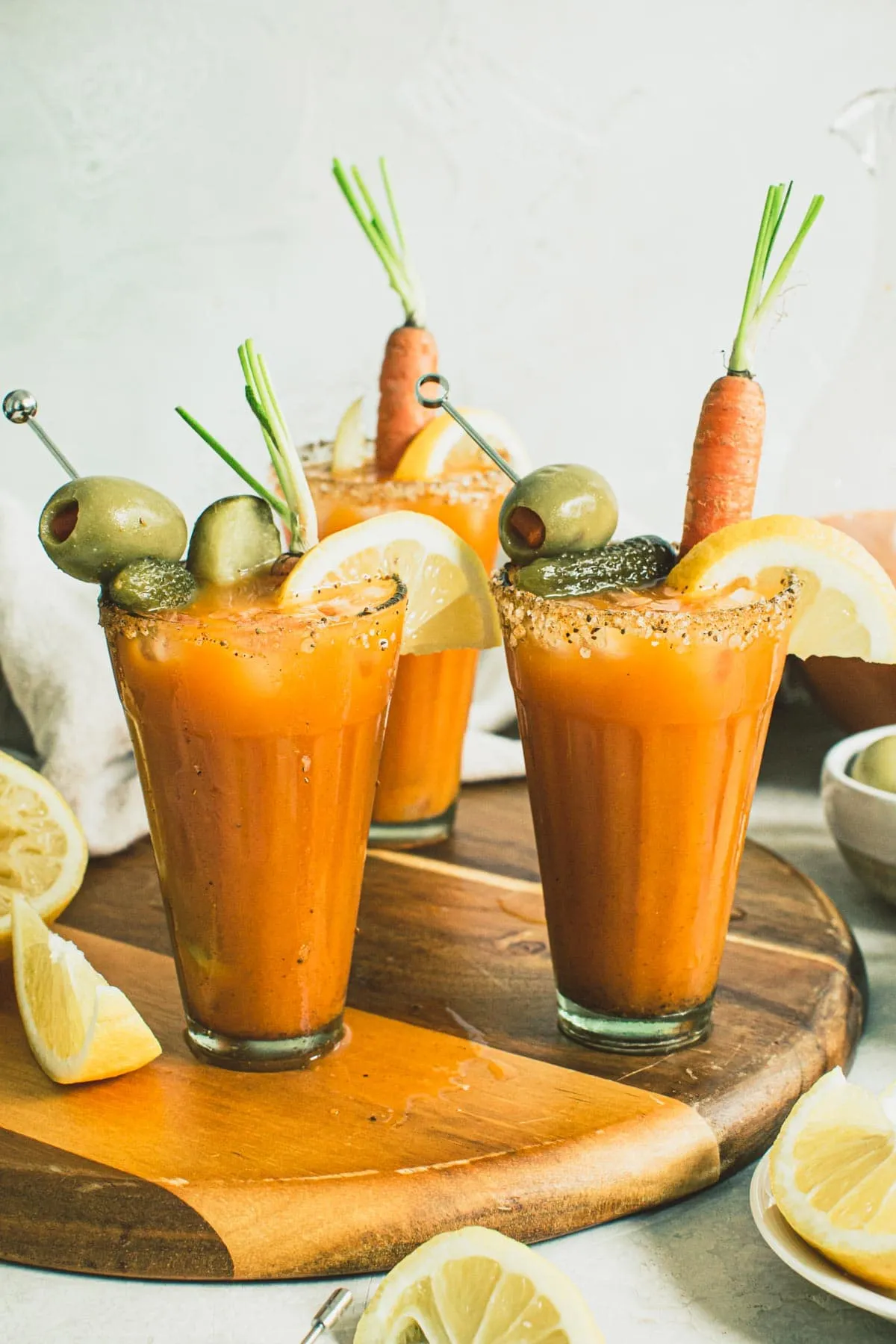 Brunch cocktails topped with garnishes sitting on a wooden board.