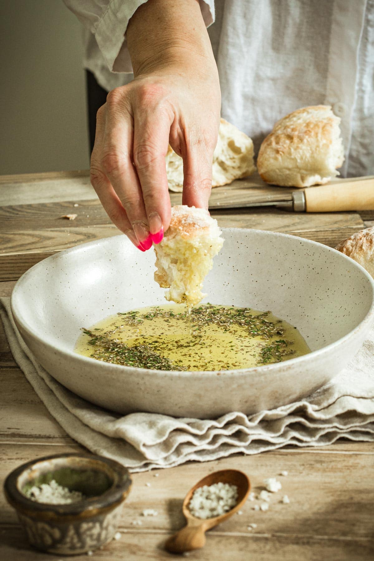 Olive oil bread dip in a bowl with hand dipping piece of bread into the oil.