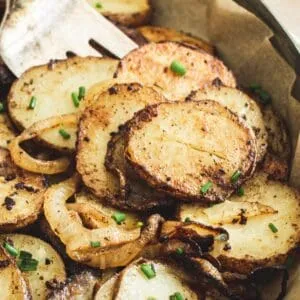 Fried potatoes and onions in serving dish with silver serving fork.