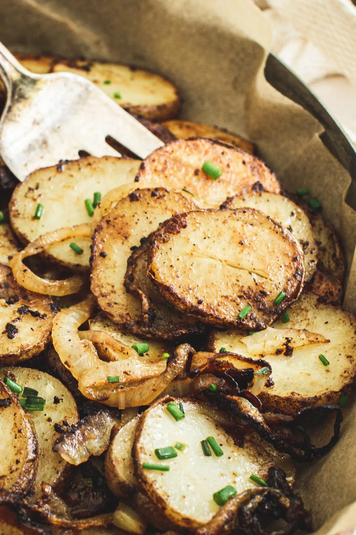 Fried potatoes and onions in serving dish with silver serving fork.