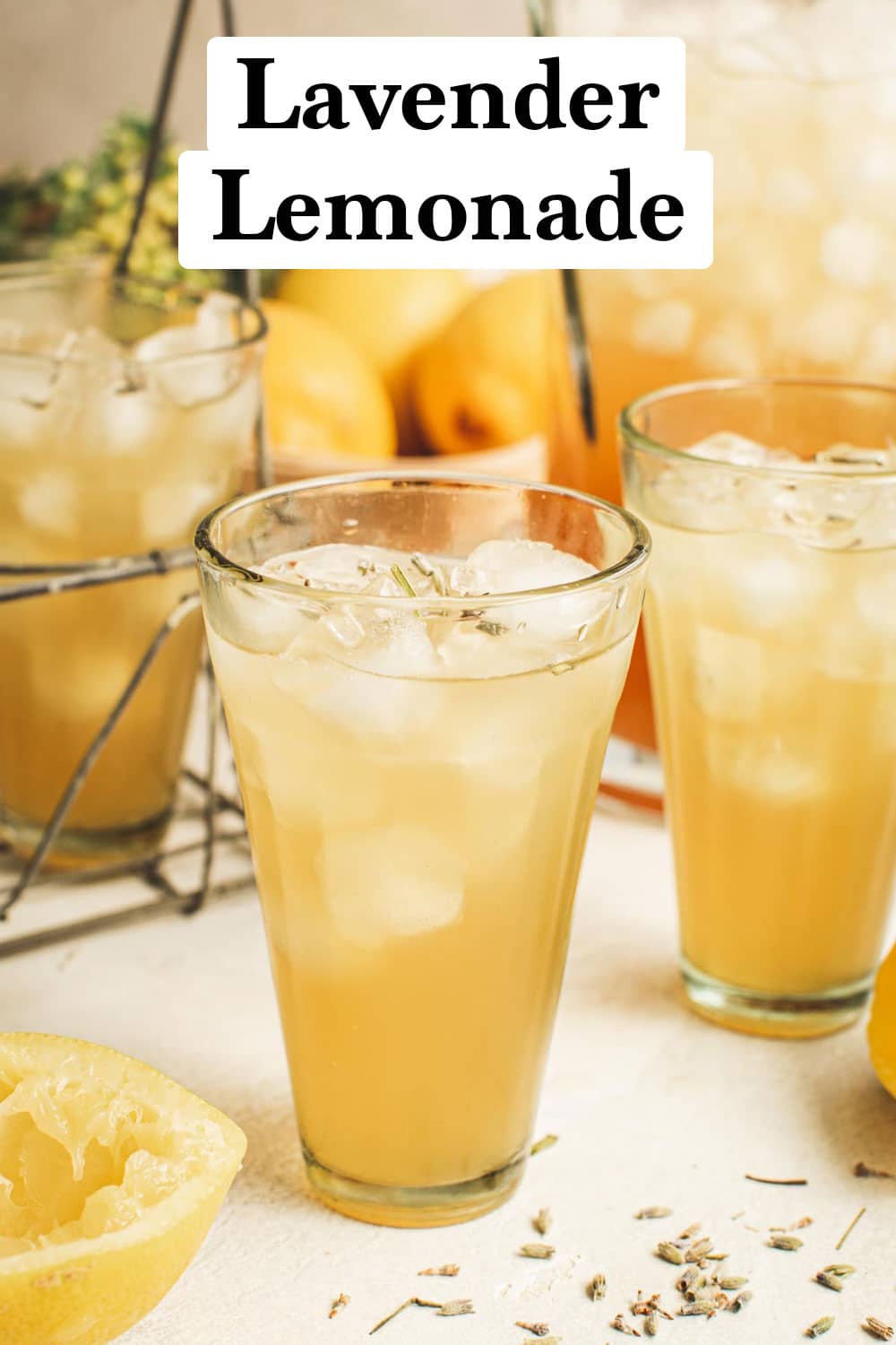 Lavender lemonade in a glass topped with fresh loose lavender tea and a pitcher behind it.