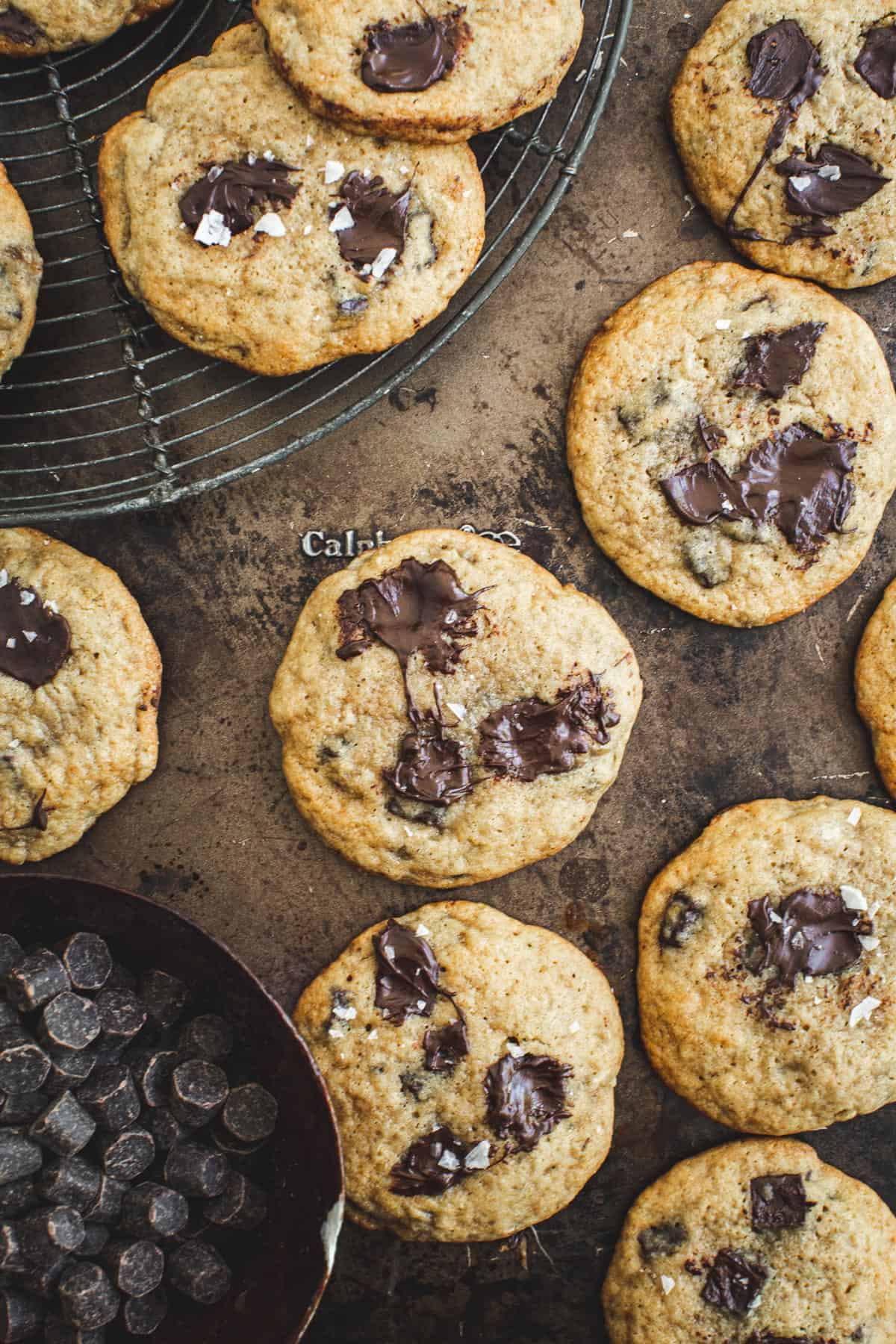 Lots of chocolate chip banana cookies on a baking sheet with a bowl full of chocolate chips next to them.
