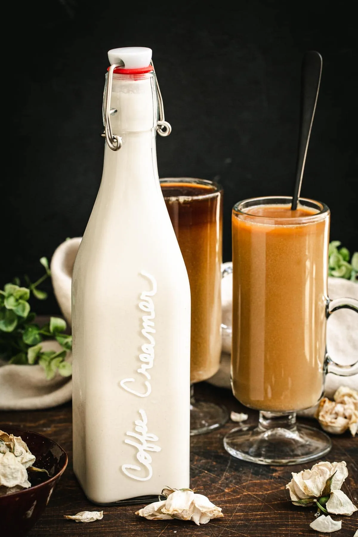 Dairy-free coffee creamer in a tall bottle next to a cup of coffee.