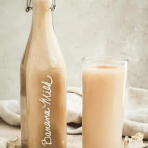 Banana milk in aa jug next to a glass filled with banana milk.