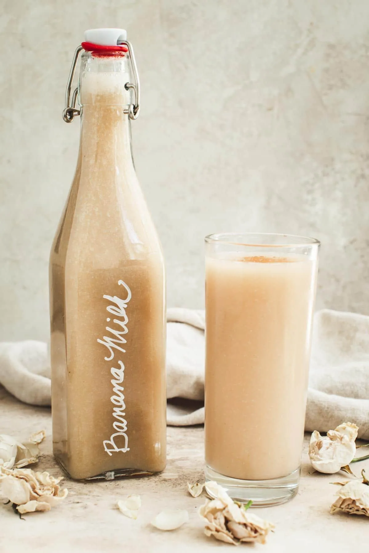 Banana milk in a glass with a jug filled with banana milk next to it.