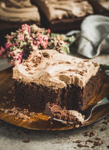 Slice of brownie cake with milk chocolate frosting and chocolate shavings on top.