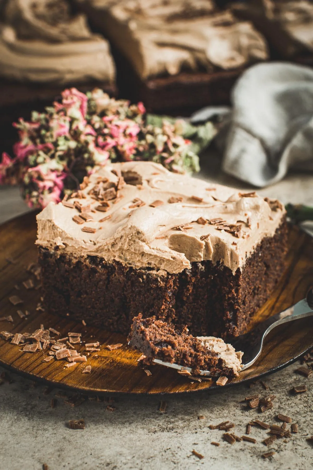 Brownie cake topped with chocolate icing on a wooden plate.