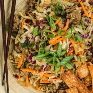 Egg roll in a bowl with crispy wanton chips and chopsticks.