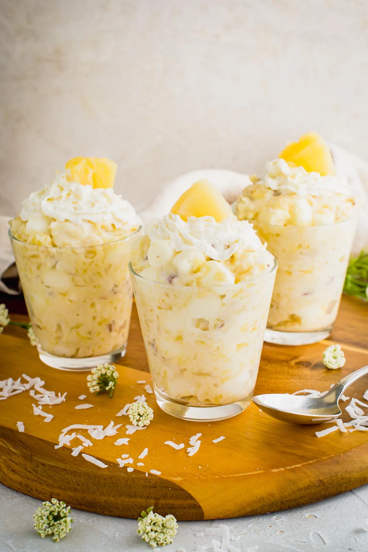 Pineapple fluff jello salad in glass cups on a wooden serving tray.
