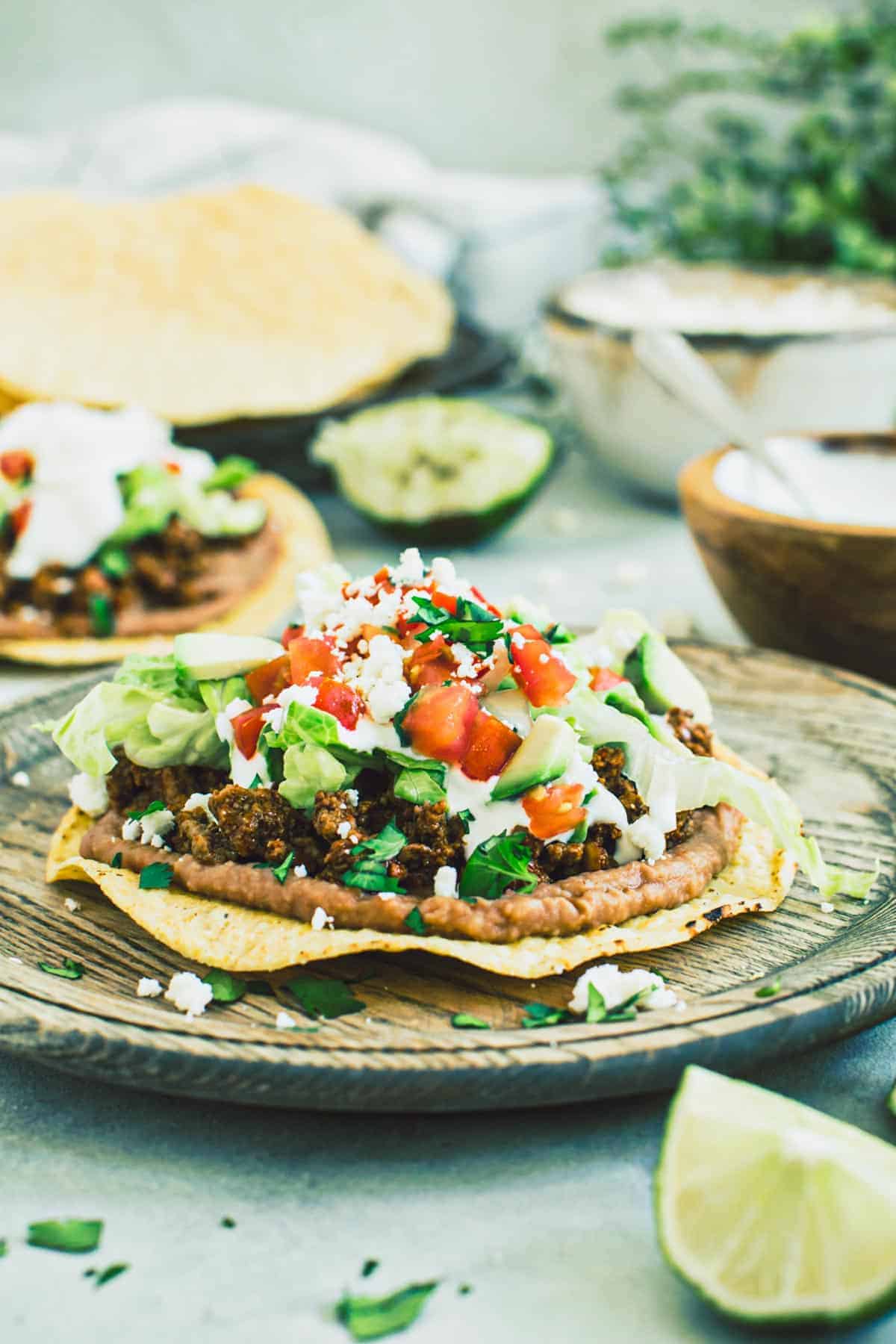 Beef tostadas topped with lettuce, tomato, and cheese on a wooden plate.