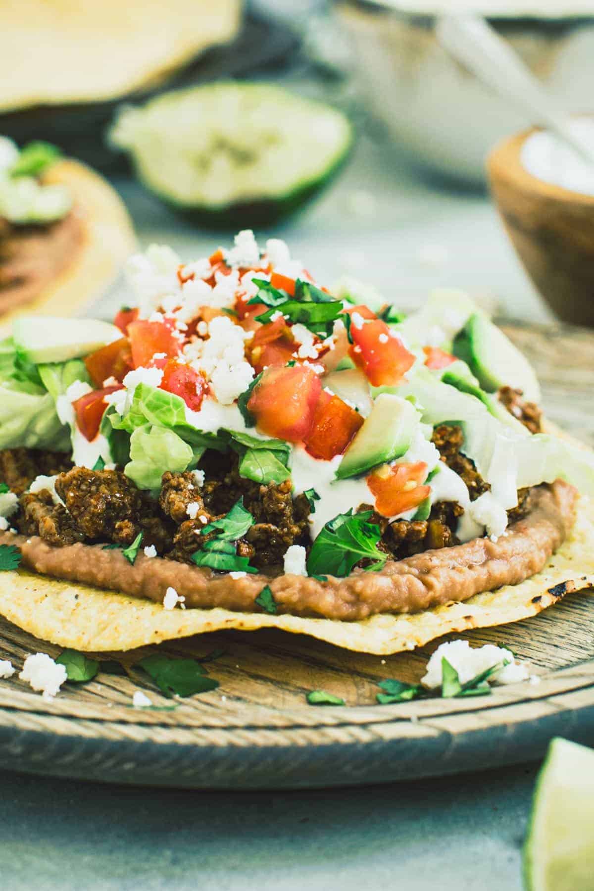 Beef tostadas with toppings on a wooden plate.