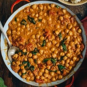 Chickpea curry in a pan with a silver serving spoon.