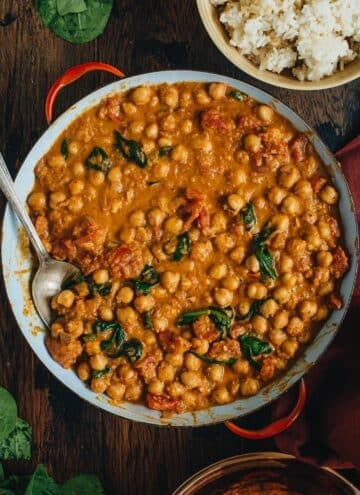 Chickpea curry in a pan with a silver serving spoon.