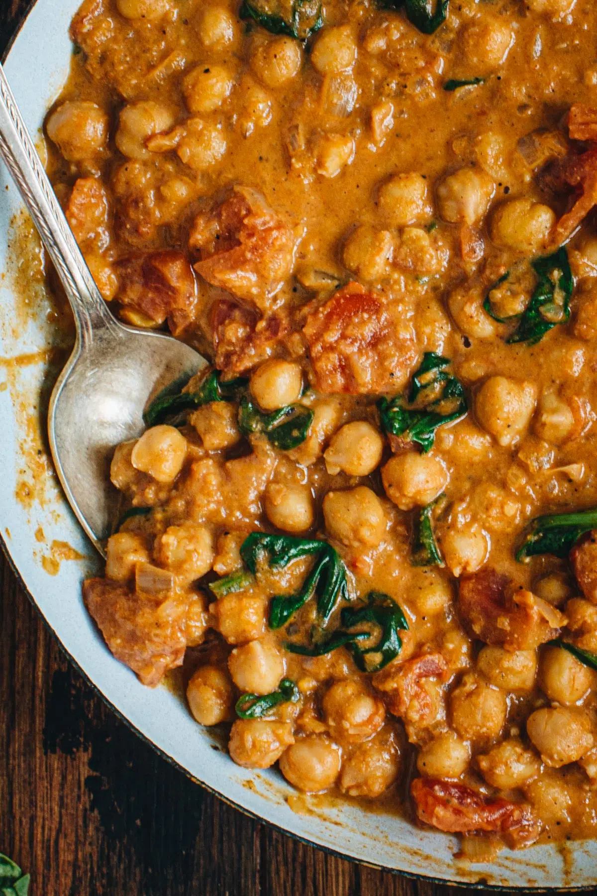 Chickpea curry in a skillet with a silver serving spoon.