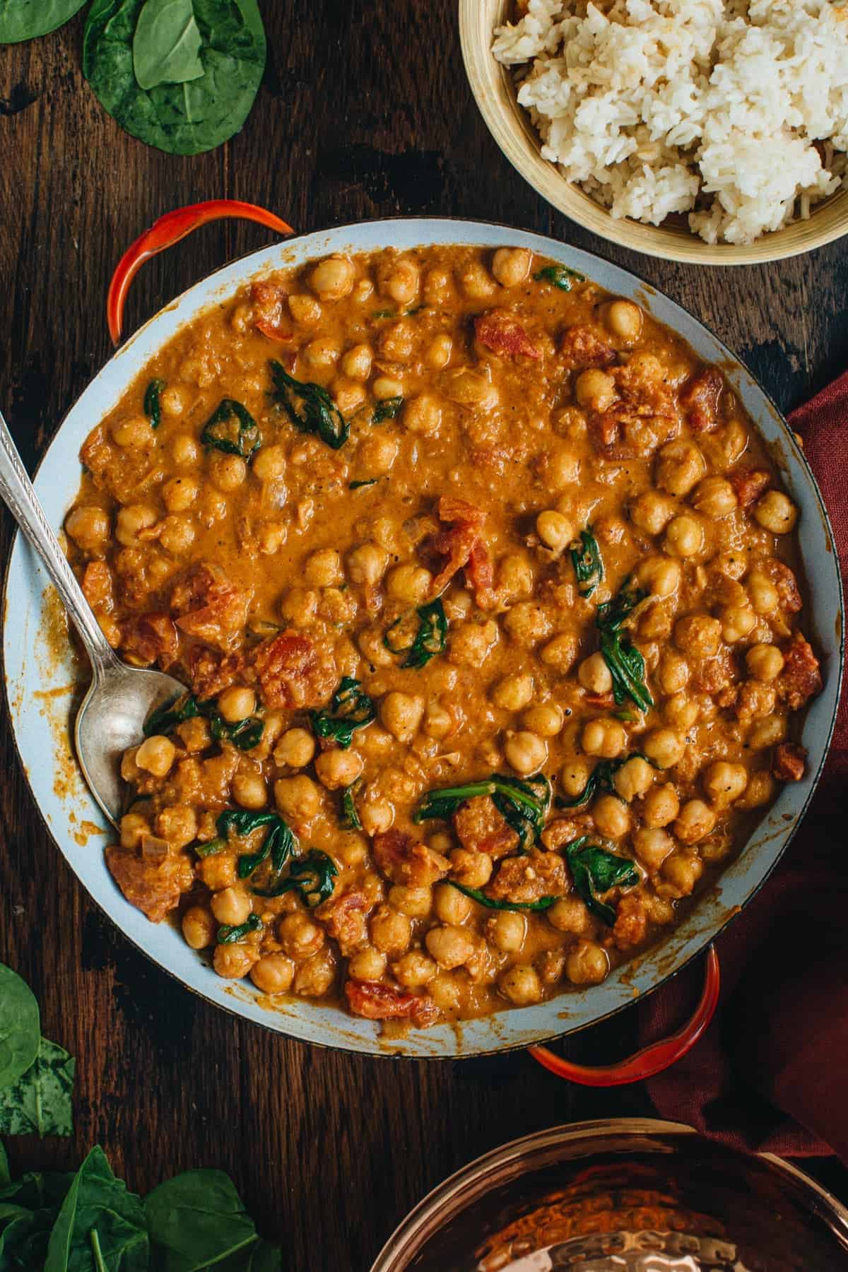 Chickpea curry in a pan with a silver serving spoon.