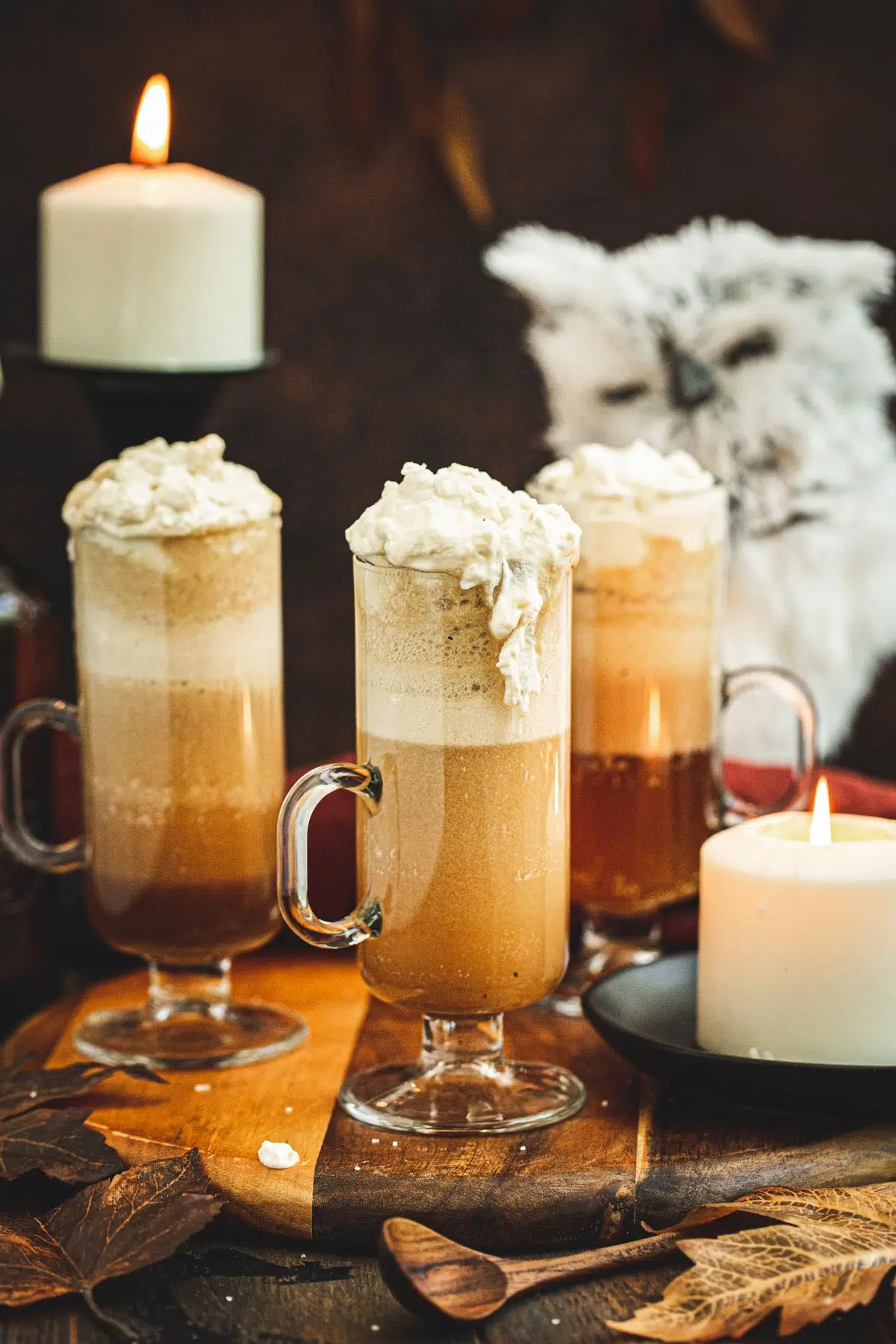 Glasses of Harry Potter butterbeer on a wooden board next to a candle.