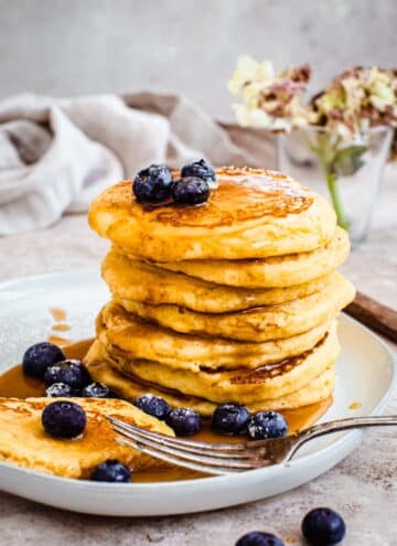 Hoe cakes stacked on a plate and drizzled with maple syrup and topped with blueberries.