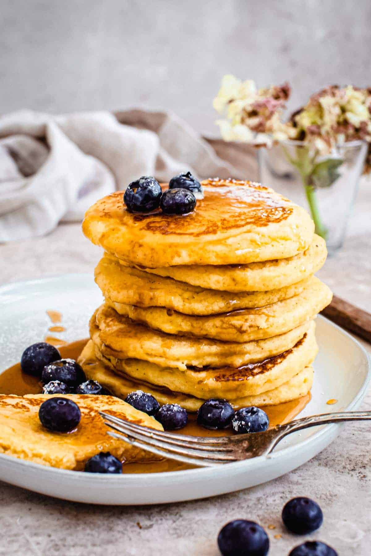 Hoe cakes stacked on a plate and drizzled with maple syrup and topped with blueberries.