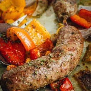 Sausage and peppers in the oven on a baking sheet.