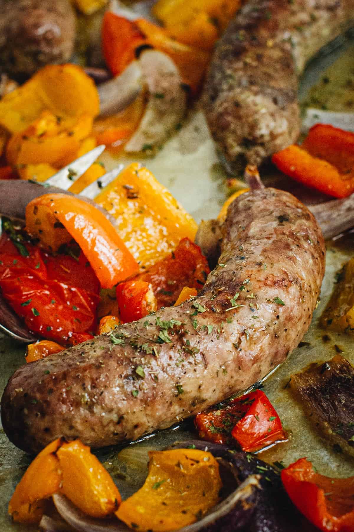 Sausage and peppers in the oven on a baking sheet and topped with fresh parsley.