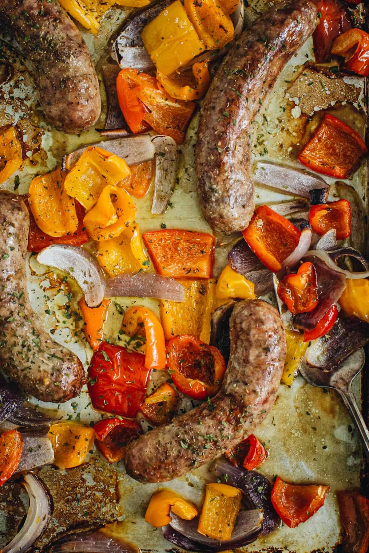 Sausage and peppers in the oven on a baking sheet.
