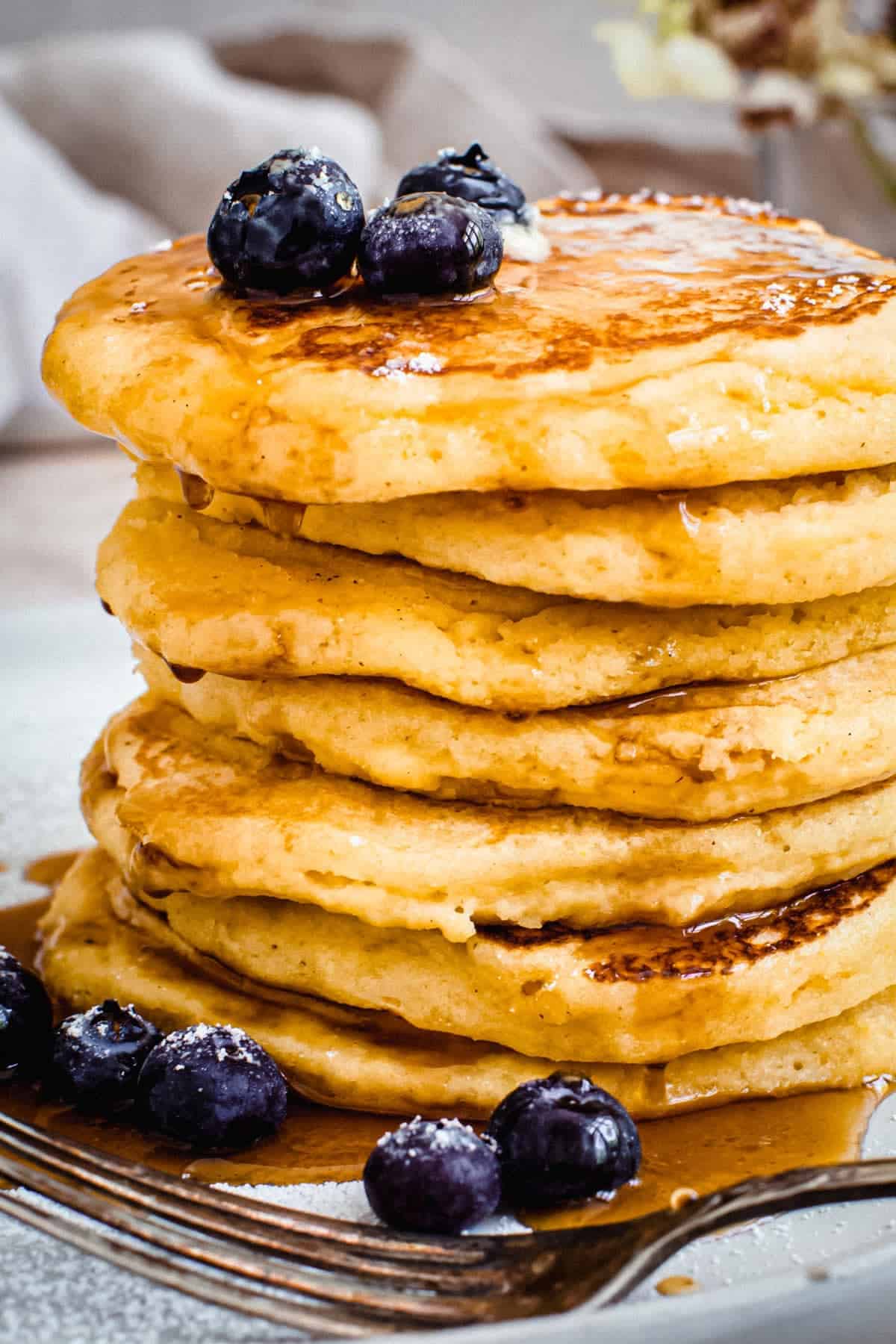 Stacked hoe cakes on a plate with maple syrup.