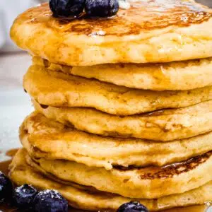Stack of Hoe Cakes topped with maple syrup and blueberries.