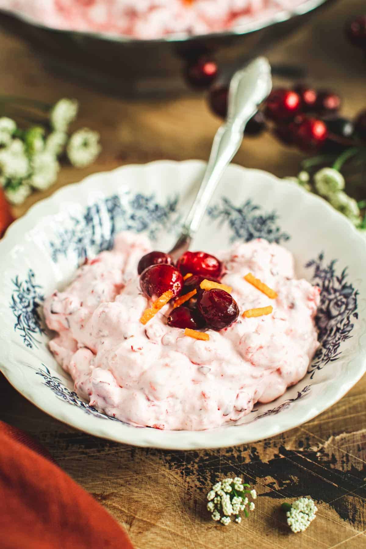 Cranberry fluff recipe in a bowl topped with fresh cranberries and orange peel.