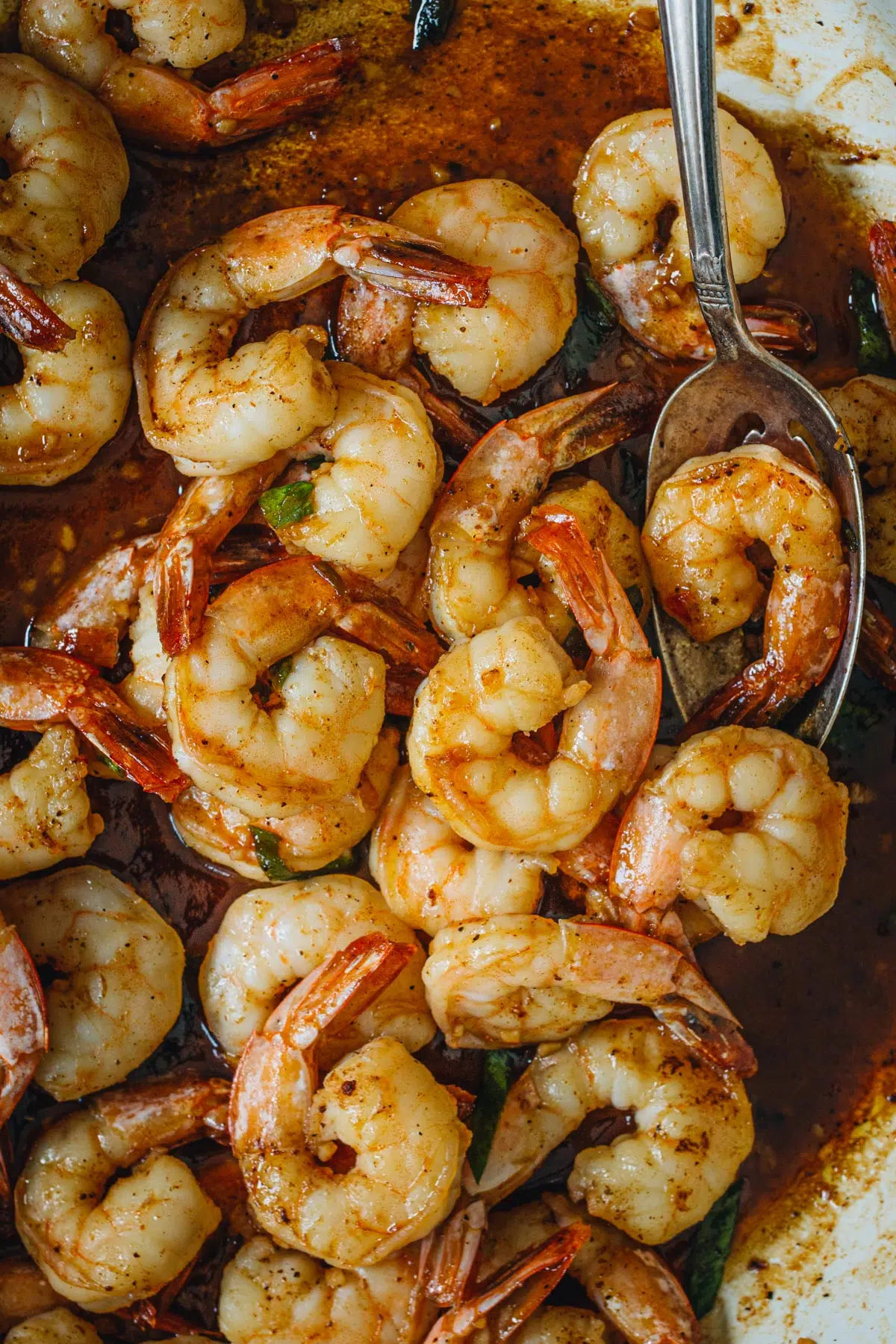 Cajun shrimp in a large skillet with a silver serving spoon.