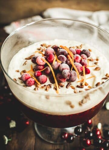 Cranberry jello salad in a trifle dish topped with fresh cranberries and orange peel.
