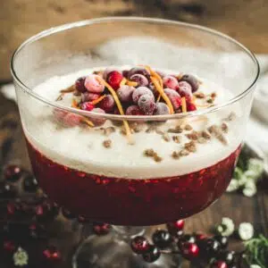 Cranberry jello salad in a trifle bowl topped with fresh cranberries and orange peel.