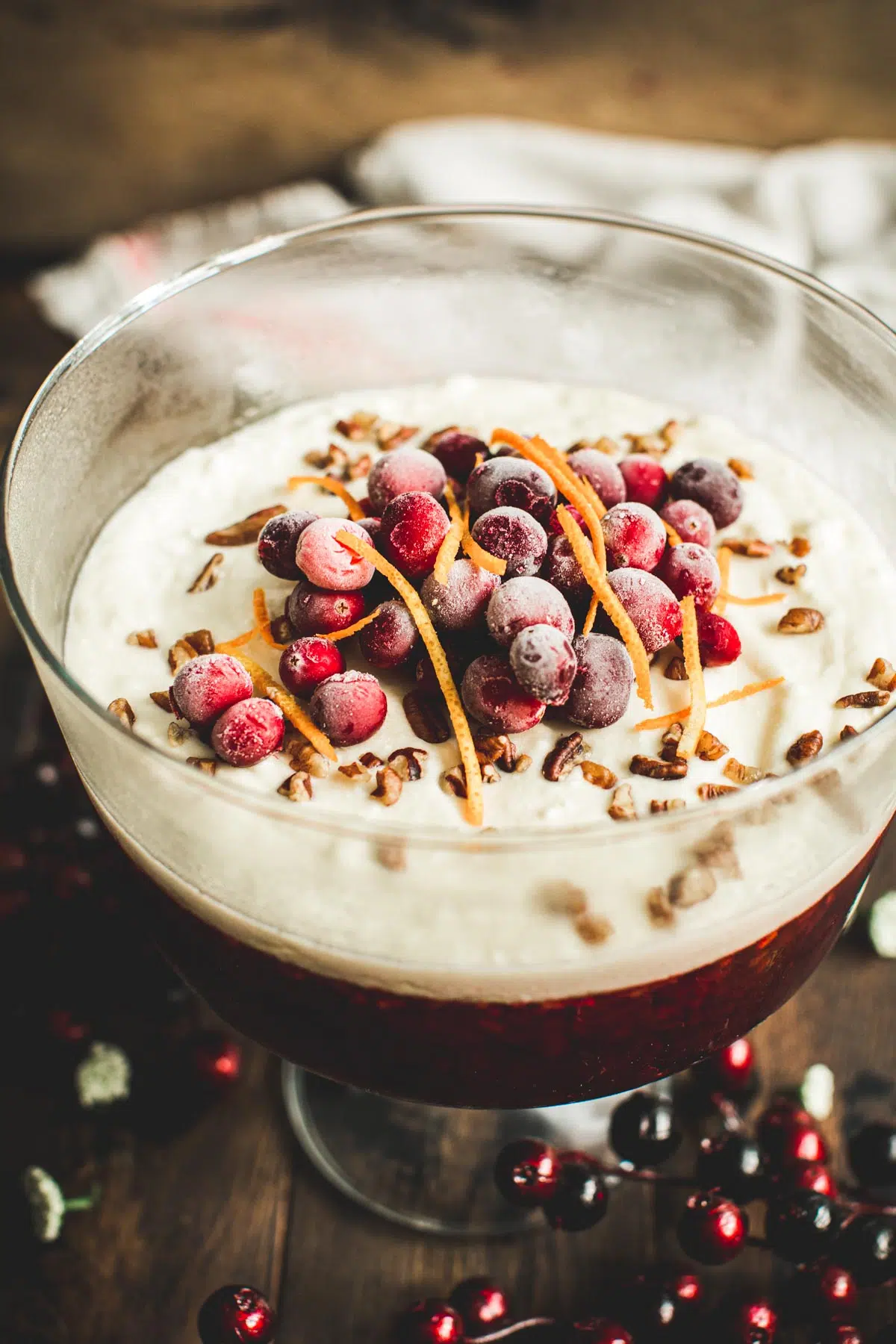 Cranberry jello salad in a trifle dish topped with fresh cranberries and orange peel.