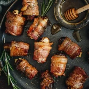 Goat cheese stuffed bacon wrapped dates with syrup in a small bowl.