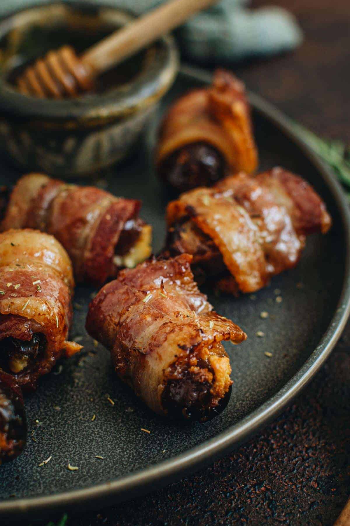 Goat cheese stuffed bacon wrapped dates on a serving plate.