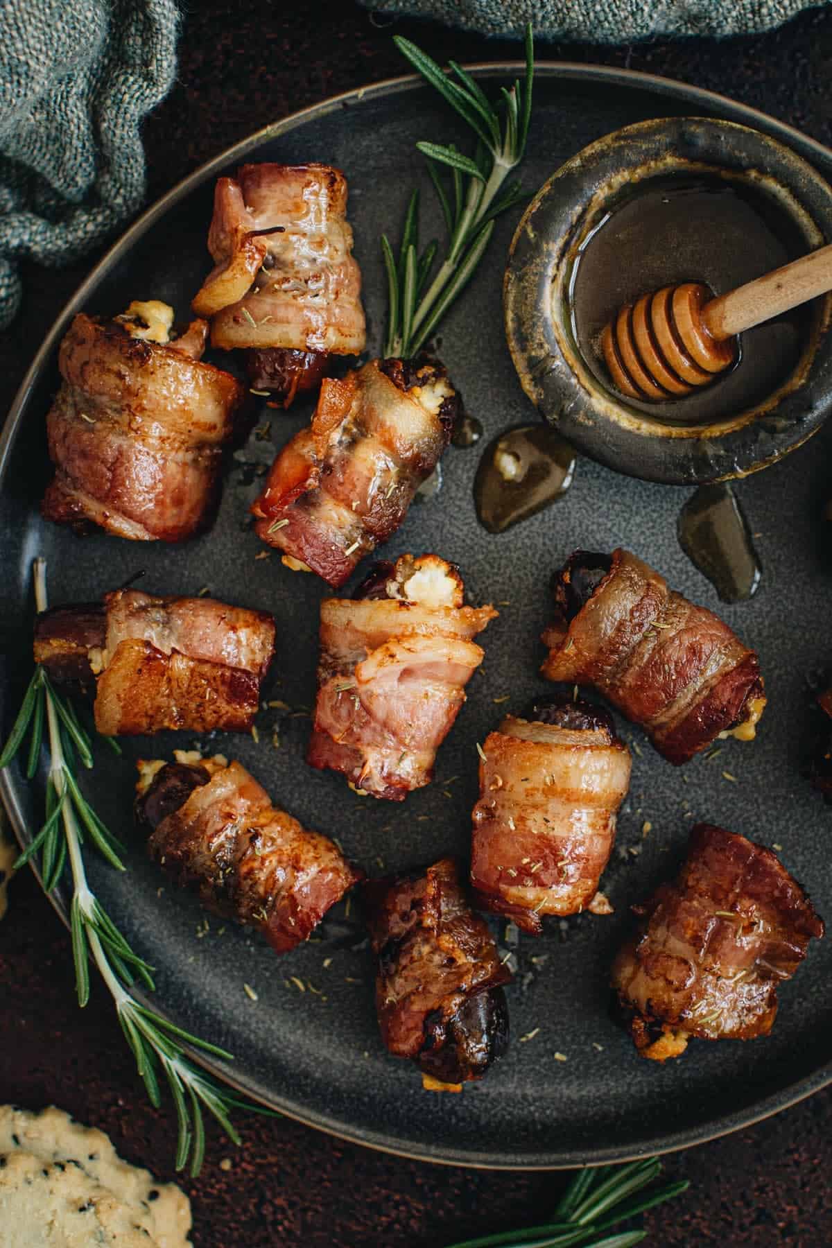 Goat cheese stuffed bacon wrapped dates on a black plate.