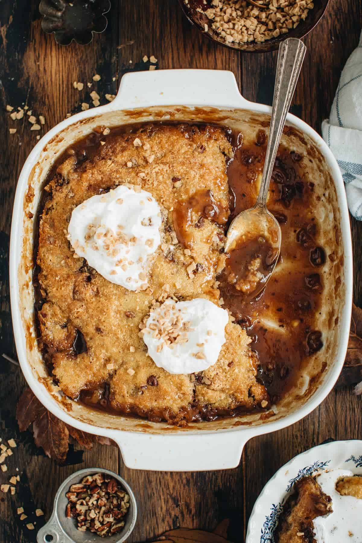 Pecan pie cobbler in a square baking dish with a silver serving spoon.