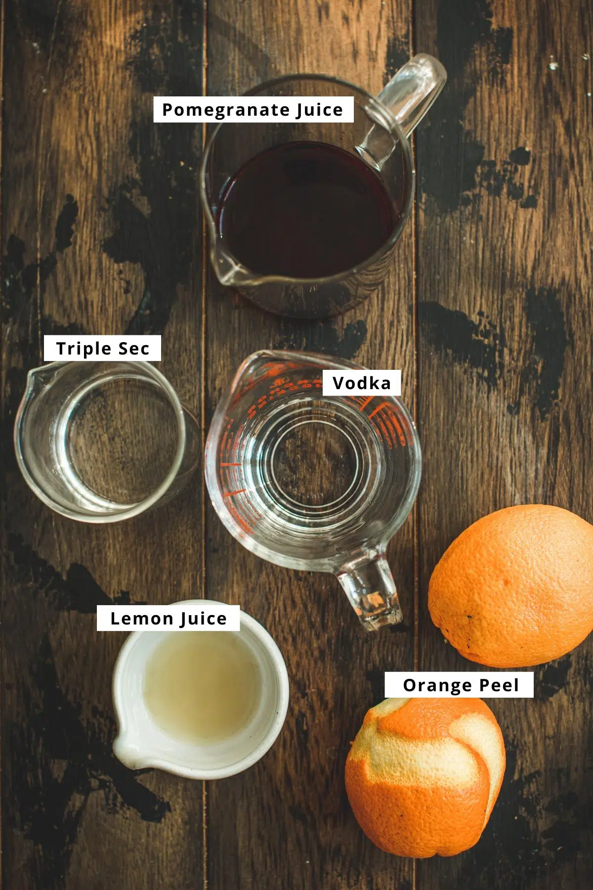 Pomegranate martini recipe ingredients on a wooden table.