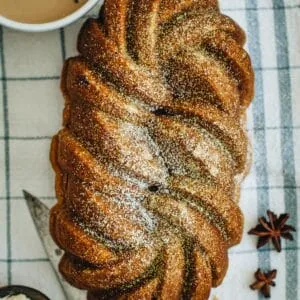 Pumpkin banana bread with powdered sugar sprinkled on top and a cup of coffee sitting next to it.