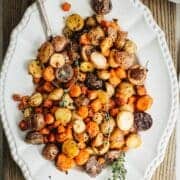 Roasted carrots and potatoes on a white platter with a silver serving spoon.