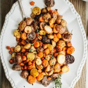Roasted carrots and potatoes on a white platter with a silver serving spoon.