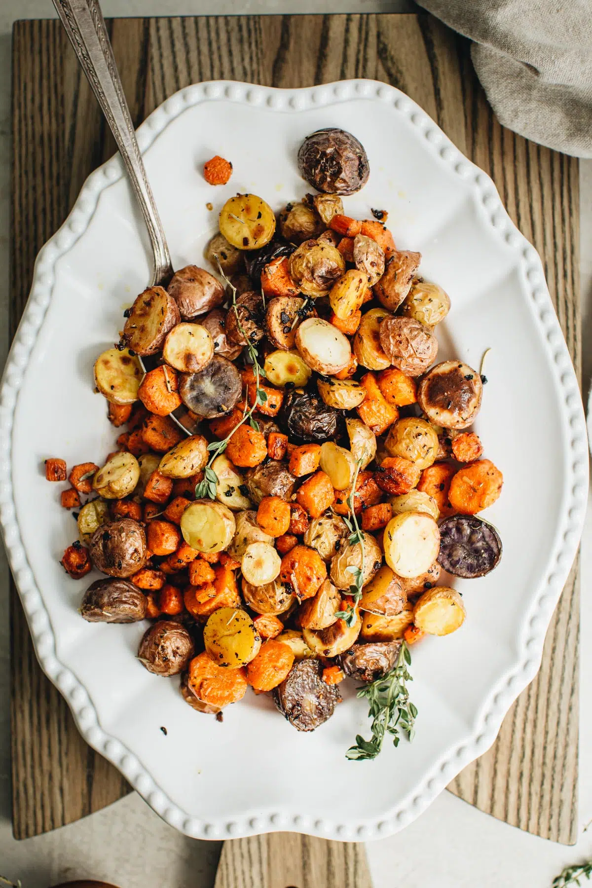 Roasted carrots and potatoes on a white platter with a silver serving spoon.