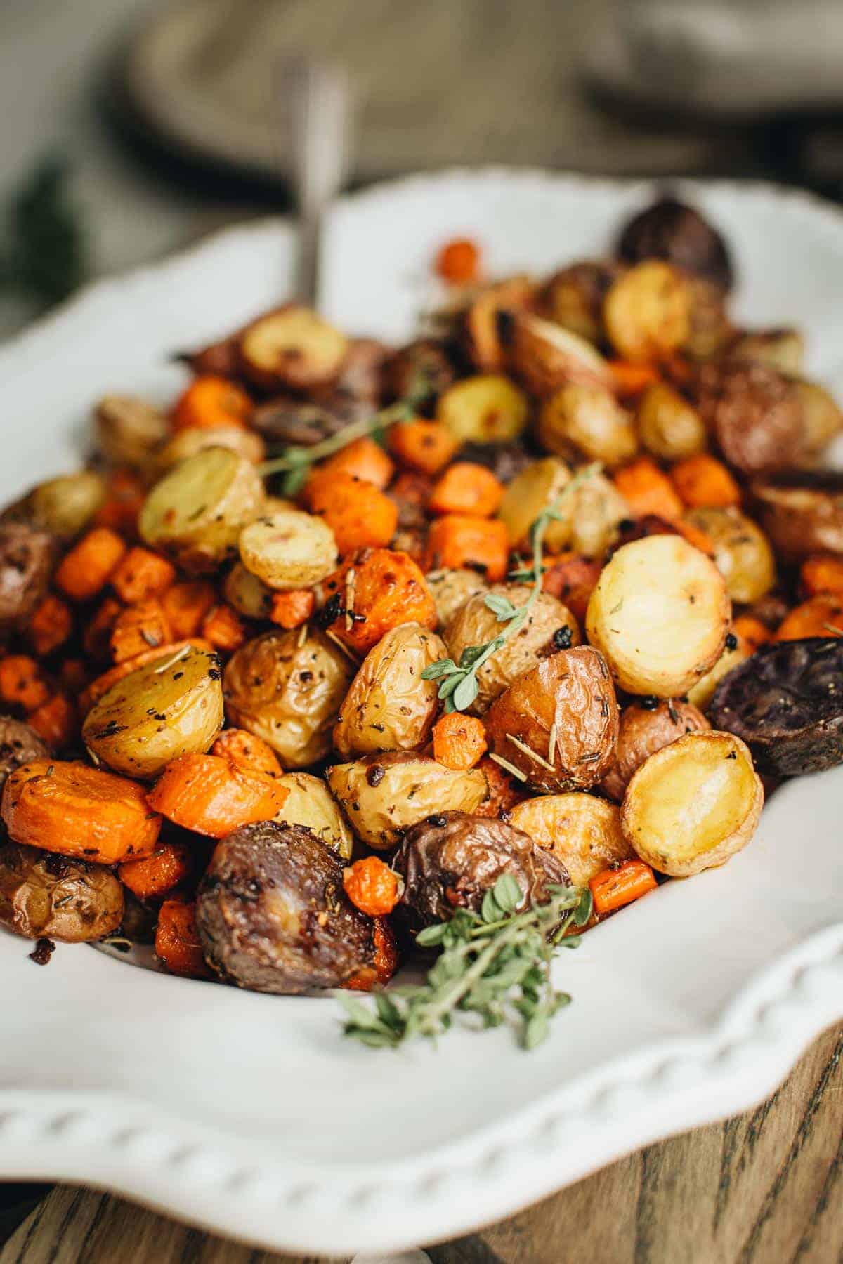 Roasted potatoes and carrots with rosemary on a white serving platter.